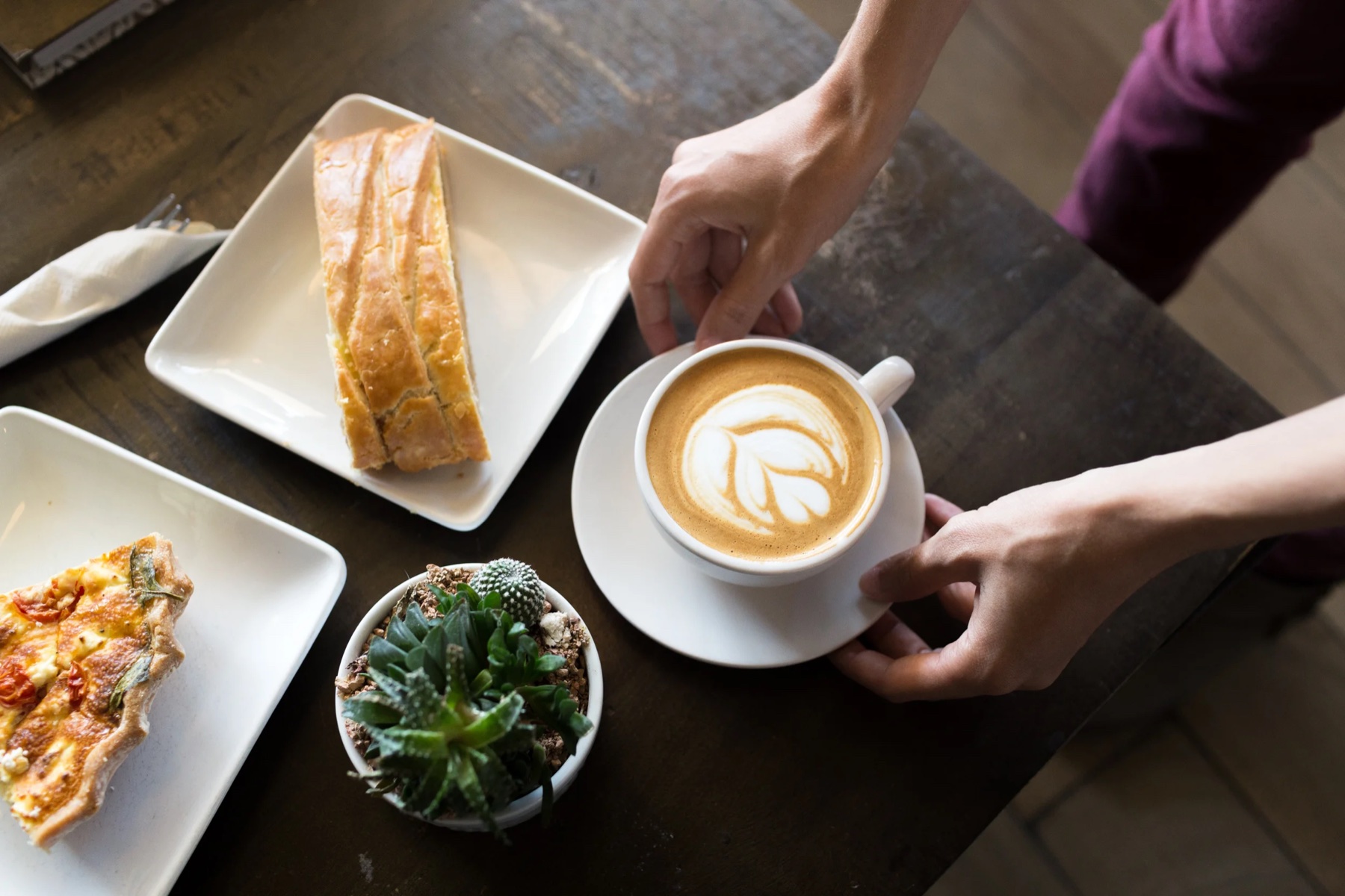 Two lattes with latte art and plates of pastry on marble, seen from above.
