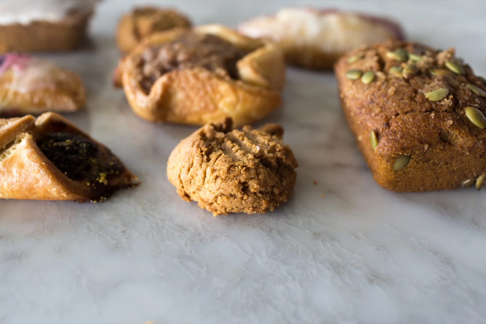 A spread of gluten-free pastries on marble: a figgy galette, a seeded loaf and a crumb-topped cookie.